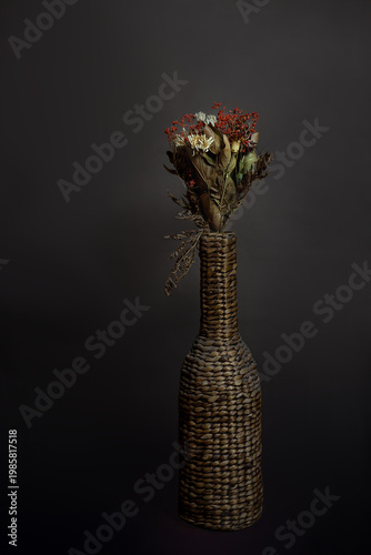 A delicate fine art studio photograph captures the quiet beauty of a dried flower arranged in an elegant woven vase.