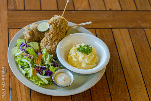 Crispy fried chicken served with creamy mashed potatoes, fresh salad, and dipping sauce on wooden table. Perfect comfort food concept for restaurant menus and food blogs