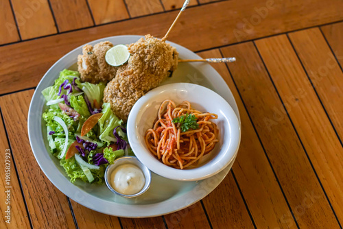 Crispy fried chicken served with spaghetti, fresh salad, and creamy dipping sauce on wooden table. Delicious comfort food meal ideal for restaurant menus, ads, and food blogs.