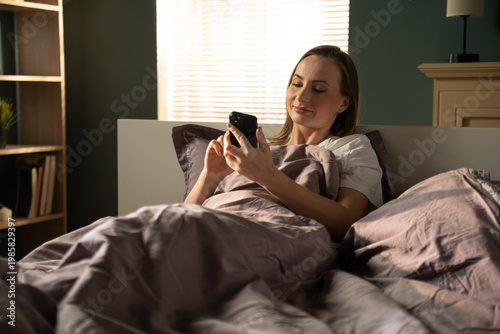 Foto Woman lying awake in bed, comfortably checking her smartphone, connecting with t