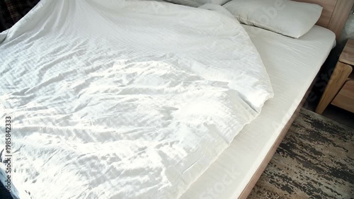 Unmade bed with white sheets and pillows in bright bedroom setting