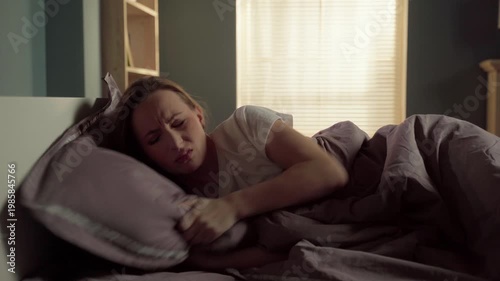Stressed young woman suffering from insomnia, struggling to find a comfortable position in bed, tossing and turning with anxiety and exhaustion during a restless night at home