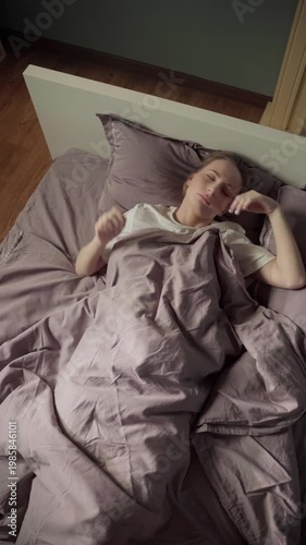 Young woman lying in bed, turning and tossing restlessly, unable to fall asleep due to anxiety, stress, insomnia, or a nightmare. Top down view of her troubled sleep in the bedroom