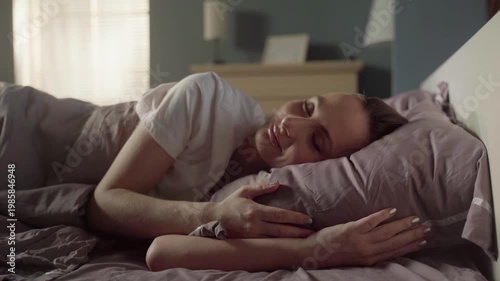 Charming young woman sleeping sweetly in her cozy bed in the morning light, enjoying a peaceful and restful sleep while hugging a soft pillow and having pleasant dreams in her bedroom