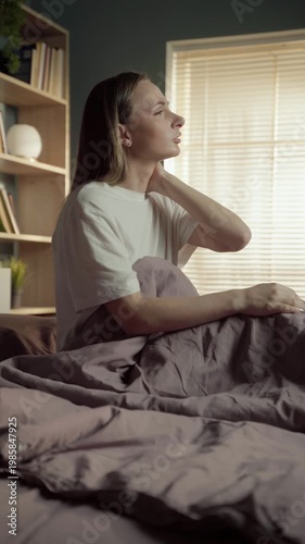 Young woman waking up in her bed and massaging her stiff neck, experiencing discomfort and muscle pain from sleeping in an awkward position or on an uncomfortable mattress and pillow