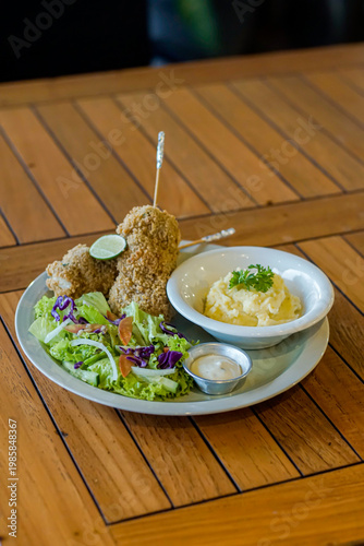 Crispy fried chicken served with creamy mashed potatoes, fresh salad, and dipping sauce on wooden table. Perfect comfort food concept for restaurant menus and food blogs.