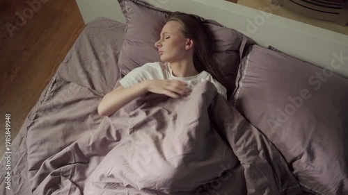 Young caucasian woman sleeping uncomfortably in her bed, tossing and turning from side to side because of a bad dream or insomnia while trying to rest in her cozy bedroom at home