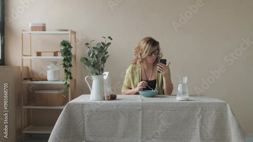 Young woman eating breakfast and using smartphone at home