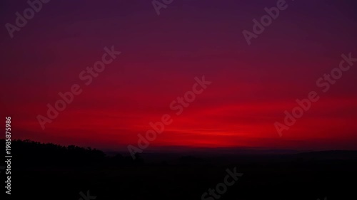 Crimson sunset fading to purple night over a silhouetted forest.