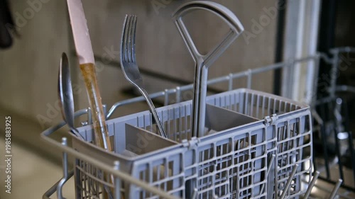 Hand placing dirty dishes into dishwasher utensil basket for cleaning