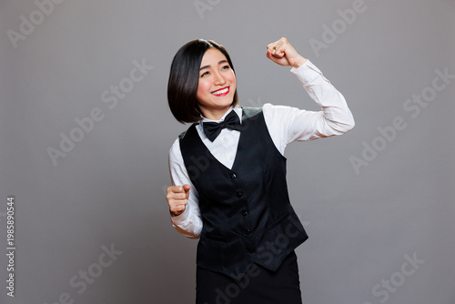 Cuadro en lienzo Cheerful asian waitress dressed in restaurant uniform dancing with joyful facial expression