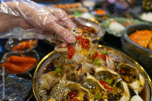 Hand with glove holding marinated crab piece over platter