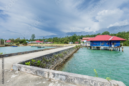 Traditional blue wooden house built on stilts over tropical turquoise water near a concrete pier