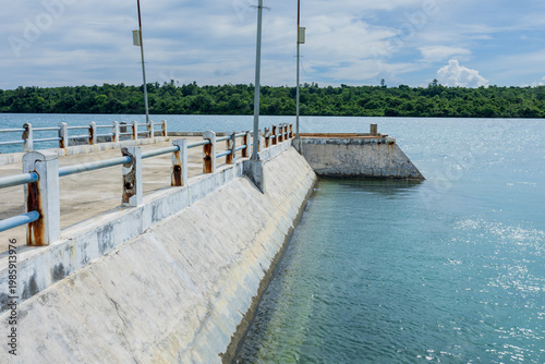 Concrete pier with solar powered street lights extending into the calm blue ocean near a tropical island
