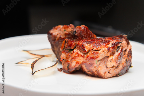 Grilled beef steak served on a white plate with garnished onion slices