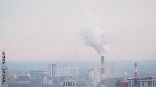 White smoke billows from a towering industrial smokestack against a hazy city skyline, illustrating urban air pollution and environmental challenges