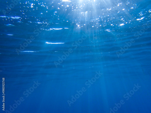 Ocean blue underwater with sunrays, Underwater Sea Deep Water Abstract Sunshine, sea wave , clean waters in summer time, Natural underwater seascape, sand on ocean floor and water surface sunlight.