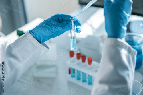 Fotografie Closeup of hands in blue gloves handling laboratory glassware and pipette with blue solution, focusing on scientific research