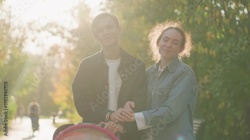 Young couple with stroller enjoying park stroll warm backlight and laughter signaling married parents enjoying family time, gentle handhold and relaxed pace through leafy avenue during golden