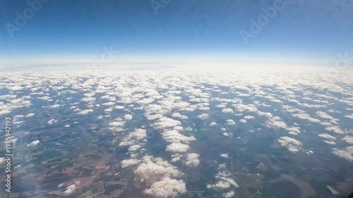 Passenger POV from airplane window showing flight above white cloud layer with deep blue sky and atmospheric gradient.