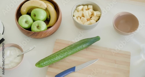 Top-down camera panning right, revealing cucumber on kitchen cutting board with knife for blending