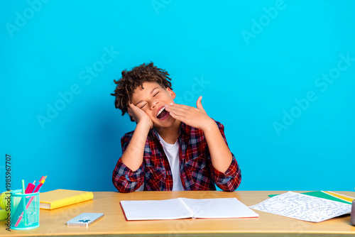 Bild auf Leinwand Tired boy student yawning at desk while doing homework and schoolwork with noteb