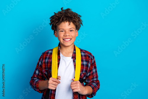 Fotografía Smiling teenage boy with yellow backpack and plaid shirt standing against bright