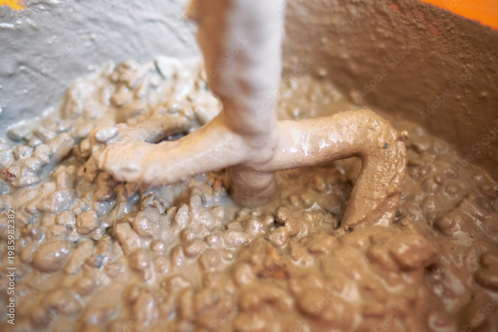 Fototapeta premium Close up of an electric paddle mixing heavy textured concrete with aggregate stones in bucket showing texture and construction material detail. Heavy duty building industrial work