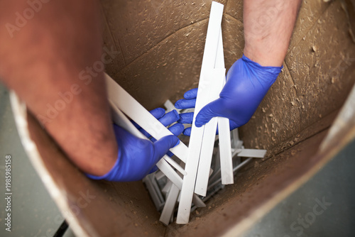 Workers hands wearing gloves handling plastic waste strips inside a cardboard container for recycling and disposal. Manufacturing and industrial plastic recycling plan. Save the planet.