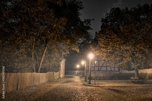 Old European cobblestone street at night with glowing lanterns and historic half-timbered house in autumn.
