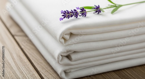 A stack of freshly laundered, crisp white bed sheets topped with a sprig of purple lavender on a wooden surface.