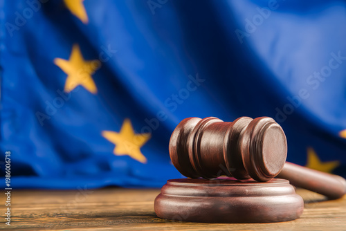 Close-up of a wooden judge gavel resting on a sound block with a blurred European Union flag, representing EU law, justice, and regulation.