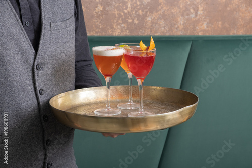 Bright alcoholic cocktails on a tray in glasses in the hands of a bartender