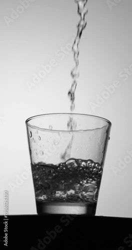 Slow-motion close-up of water pouring into a clear glass, creating dense bubbles and swirling turbulence against a clean minimal background with copy space