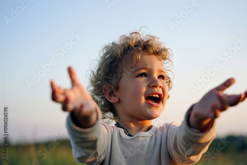 A young child with curly hair expresses joy with outstretched arms in a serene grassy landscape under blue sky. Generative AI.