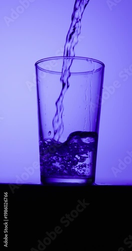Slow-motion water stream pouring into a clear glass, creating bubbles and ripples under deep blue lighting with a smooth gradient background and copy space