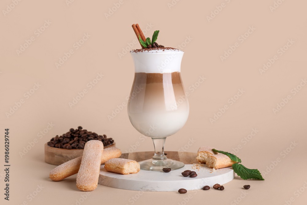Obraz premium Glass of tasty Tiramisu cocktail with coffee beans, savoiardi, cinnamon stick and mint leaves on beige background