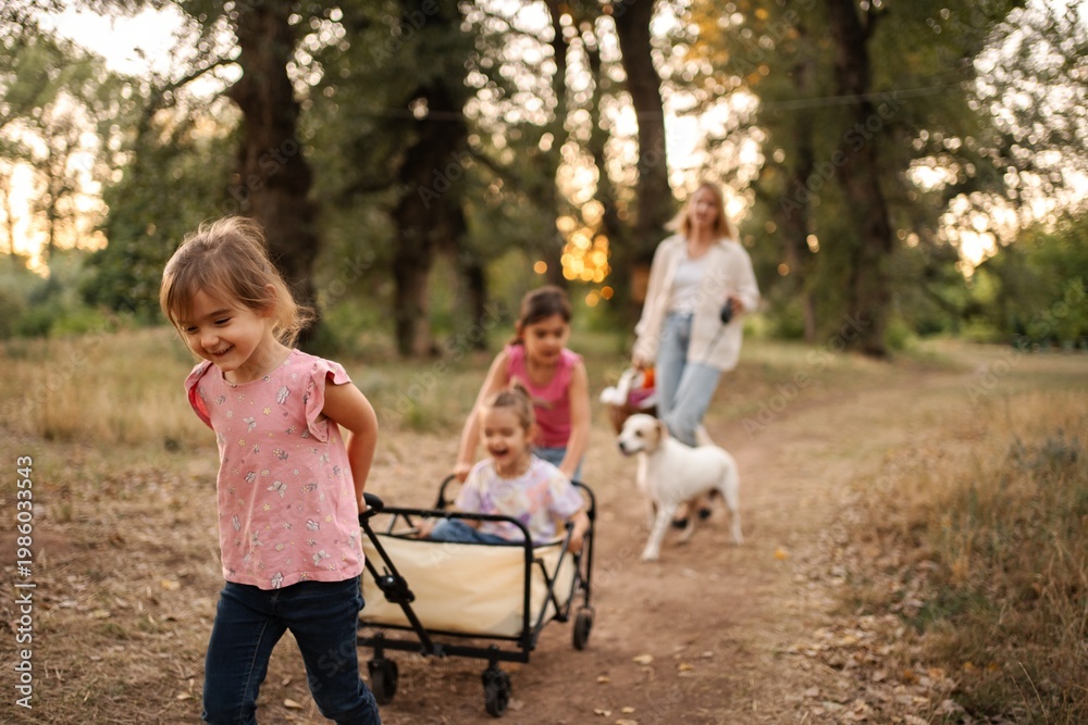 Fototapeta premium Happy children pulling wagon with their twin sisters in a forest path