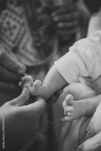 Sacrament of baptism in an Orthodox church. A priest uses a special brush for holy anointing on a baby's tiny foot, symbolizing a spiritual blessing and initiation into faith. Black and white photo.