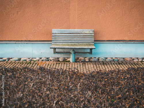 Bench sits in front of a wall in Gothenburg, Sweden on a sunny day with stones and dry grass around