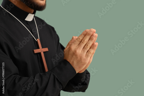 Bild auf Leinwand Young priest with wooden cross praying on green background, closeup
