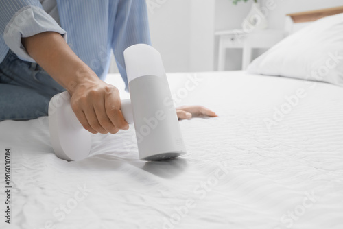 Fotografie Young woman steaming bed sheet with modern garment steamer at home, closeup
