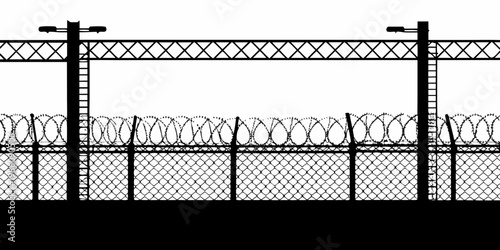 Black silhouette of a security fence with barbed wire atop a wall
