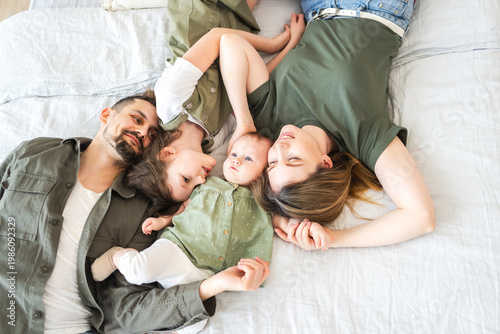 Happy family at home. Mother father two children daughters relaxing in bed indoor. Mom dad parents kids girls relax playing hugging having fun together. Family smiling laughing enjoying tender moment
