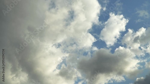 Low cumulus and stratocumulus clouds drift across a bright blue sky. Shifting formations create light and dark cloud hues, signaling a change in weather patterns over a panoramic wide shot. 