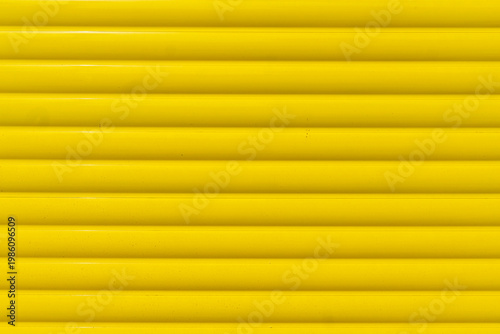 A full frame texture of a brightly painted yellow metal roller shutter, with horizontal slats.