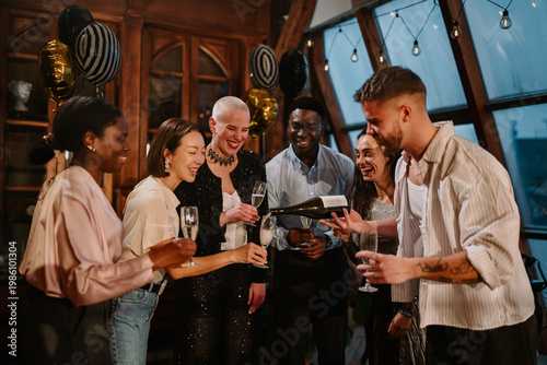 Schilderij op canvas Diverse friends enjoying a celebration, pouring champagne into glasses at an eve