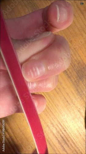 Close up of a person filing their natural fingernails with a red emery board for shaping and grooming, promoting self care hygiene and personal beauty treatment