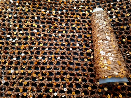 Brown sequin mesh fabric texture with gold sequin thread spool, luxury fashion textile material for sewing and embellishment close-up
