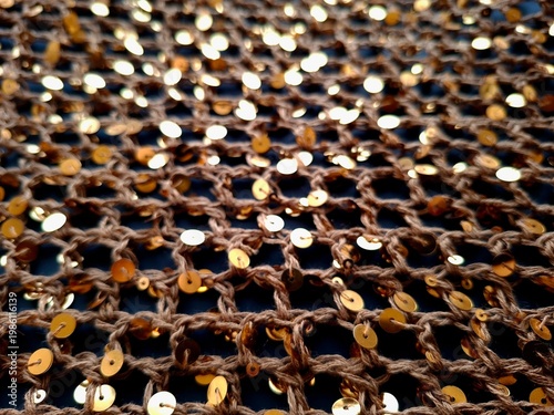 Detailed view of bronze crochet netting with embedded gold sequins, shimmering fabric texture for luxury fashion design and party wear concepts
